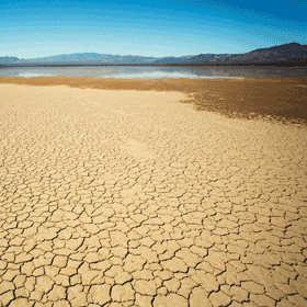 A photo of dried, cracked sand with an eroded shoreline in the distance